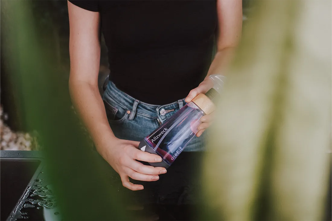 Blick durch eine Pflanze auf die WingGuard Reinigungsflasche, gefüllt mit Allzweckreiniger aus Putzmittel-Tab.