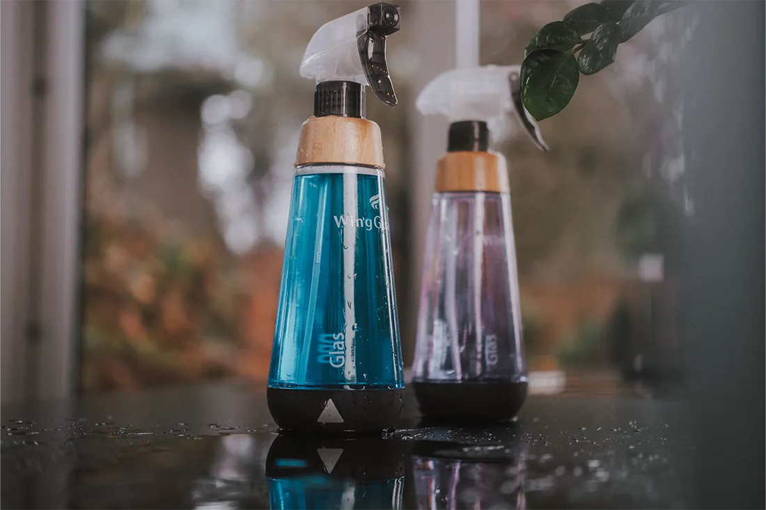 Man sieht zwei WingGuard Reinigungsflaschen auf einer nassen Arbeitsfläche, jeweils gefüllt mit nachhaltigem Tab-Glasreiniger und Tab-Allzweckreiniger.